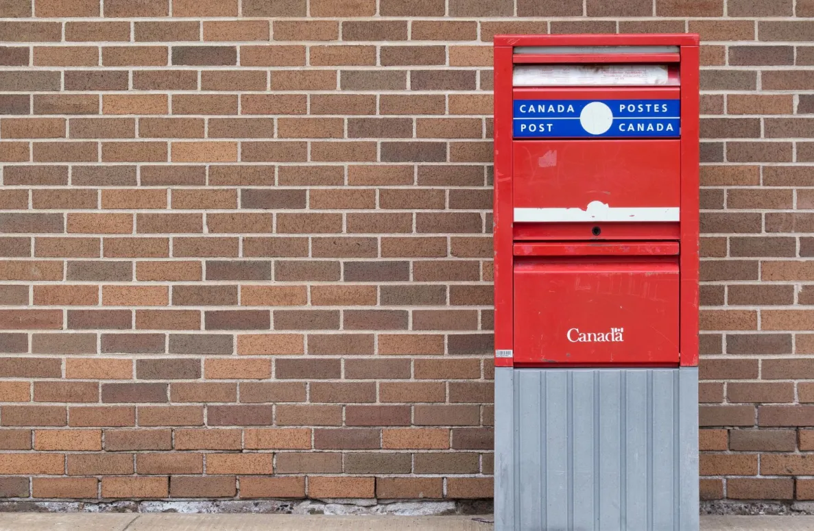 A red Canada post mailbox placed in front of a brick wall.