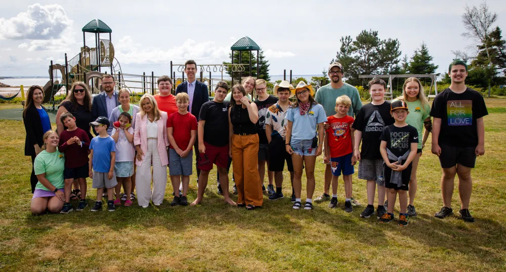 Adults and youth stand in front of the playground at Camp Gencheff on a sunny day.