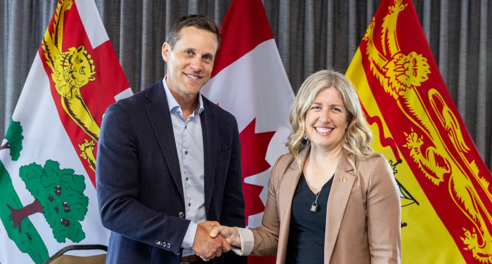 The Premiers shake hands in front of the PEI, New Brunswick and Canadian flags.