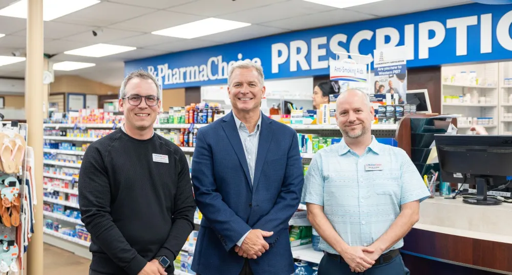 Deux pharmaciens masculins et le ministre se tiennent côte à côte devant un comptoir de pharmacie.