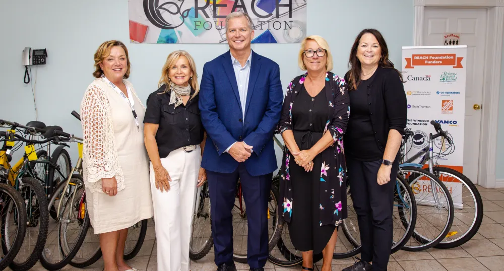 Five people stand in front of a Reach Foundation poster.