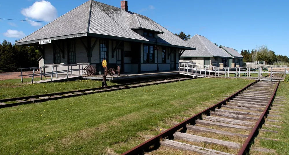 The Elmira train station stands behind train tracks on a sunny, blue-sky day.