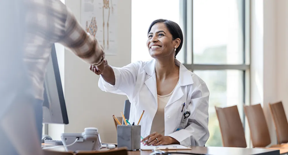 Find a Family Doctor or Nurse Practitioner Smiling female doctor sitting at their desk greets patient by shaking their hand