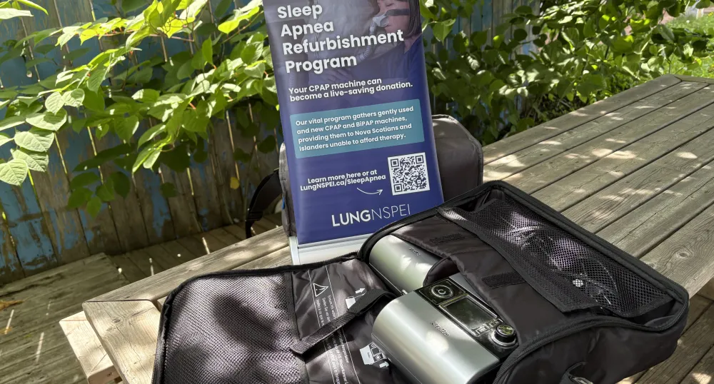 A sleep apnea machine on a picnic table outside, with green foliage in the background.