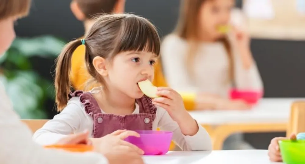 little girl sitting at a table eating a banana