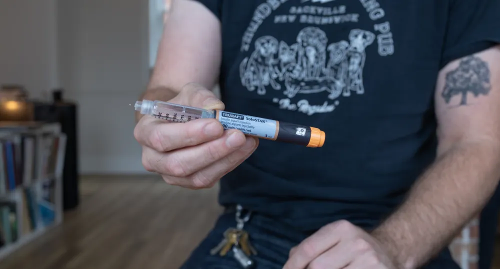 A man holds a cylinder of medicine, reading the text you can see it is an insulin injection