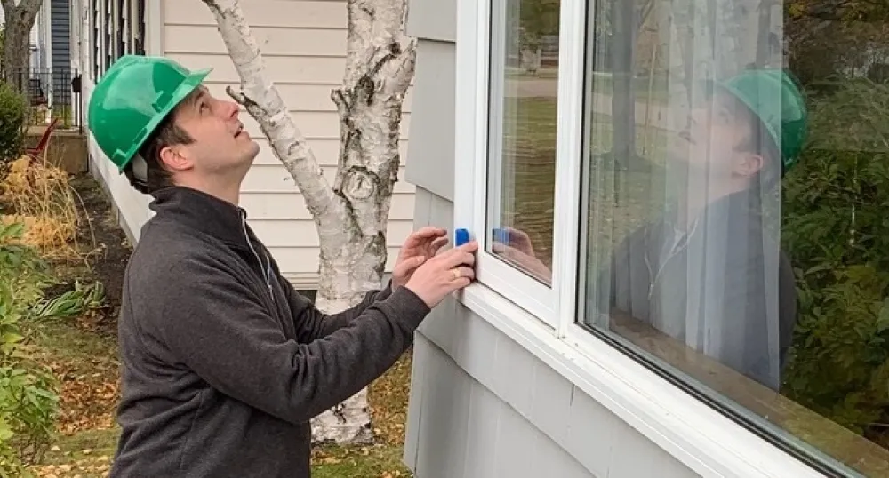 Male home energy inspector takes a reading at a picture window