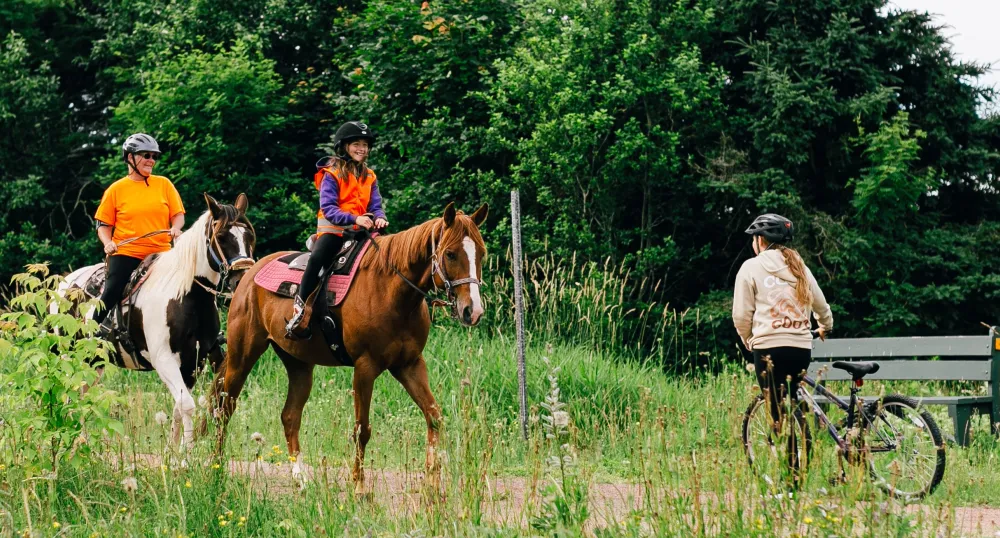 Someone pushes a bike past two equestrians on the Confederation Trail