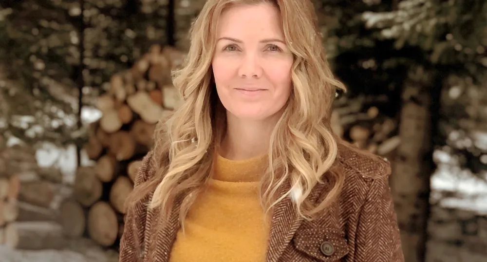 A smiling woman with long hair and a cozy wool coat in a wintery scene