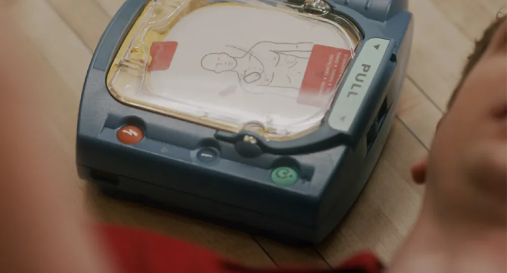 AED … IT’S BLEEPING EASY. AED sitting on floor next to man.