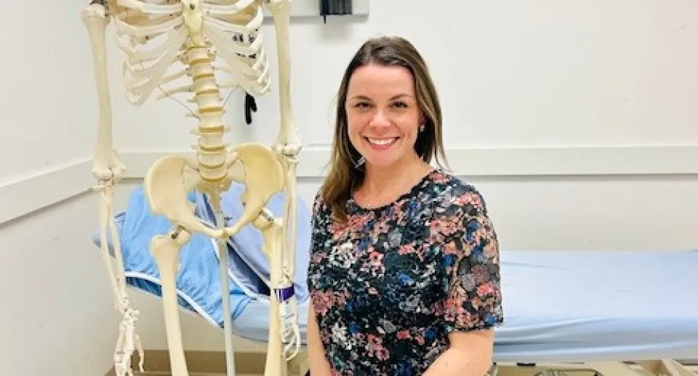A woman, a physiotherapist, poses in front of a skeleton 