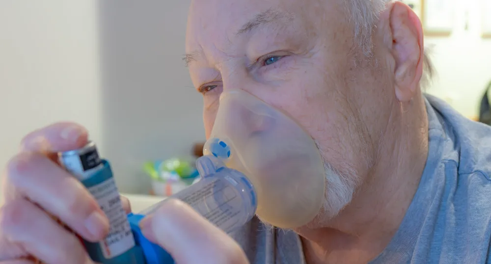 An older man uses an inhaler