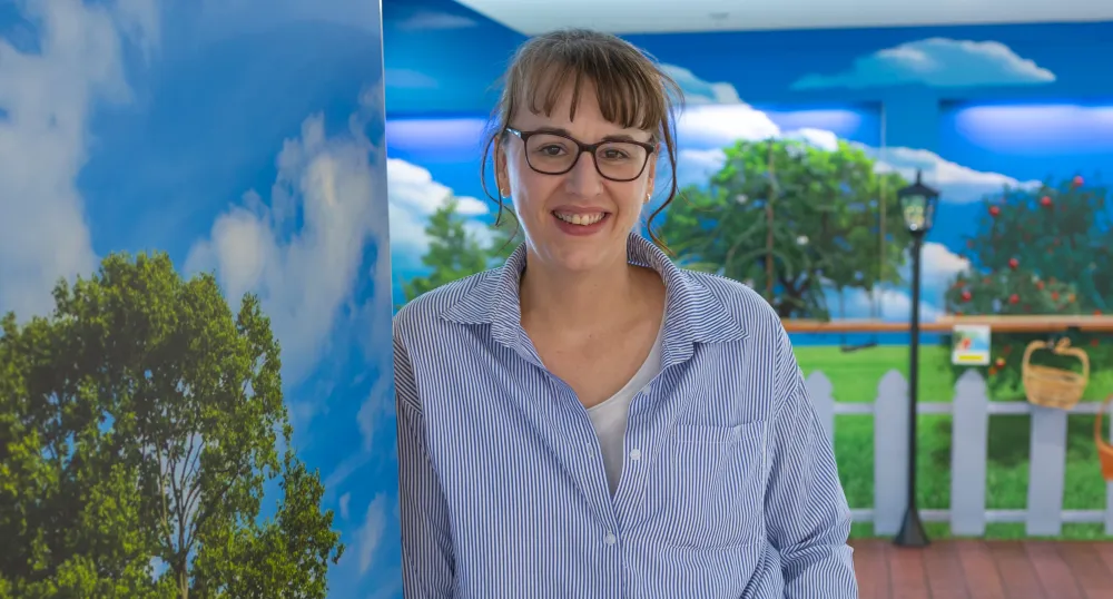 A smiling woman standing in a room painted with bright walls looking like a sunny orchard