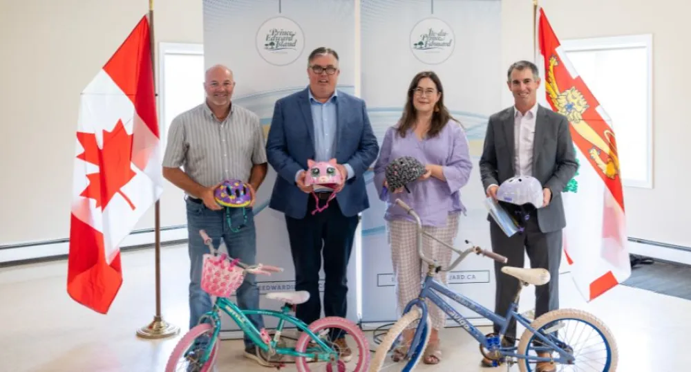 Communities receive funding for active transportation projects image of four people standing shoulder to shoulder inside a room in front of a display banner each holding a cycling helmet