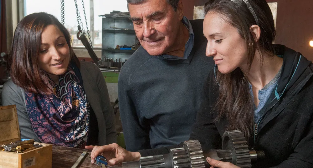 Three people looking at a machine part and measuring its size.