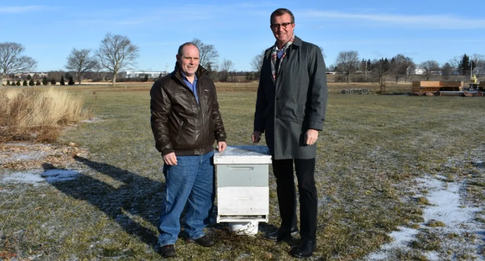 Photo shows two men standing on either side of a box-shaped beehive.