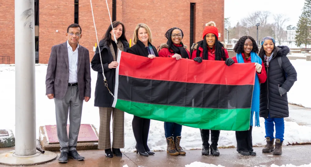 Statement by Premier Dennis King for Black History Month image of a group of people standing shoulder to shoulder holding a flag before it is raised up a flagpole
