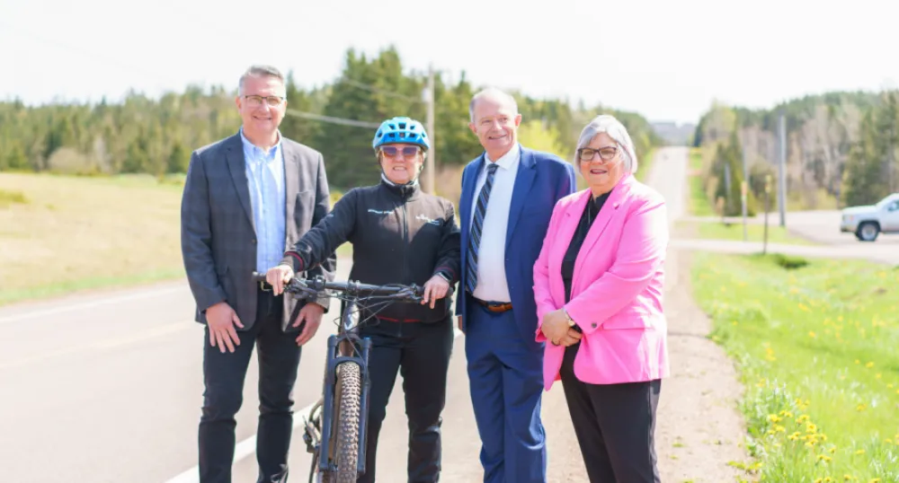 Canada and Prince Edward Island partner to invest in active transportation corridors across the province image of four peole standing shoulder to shoulder beside a road and one person holding onto a bicycle