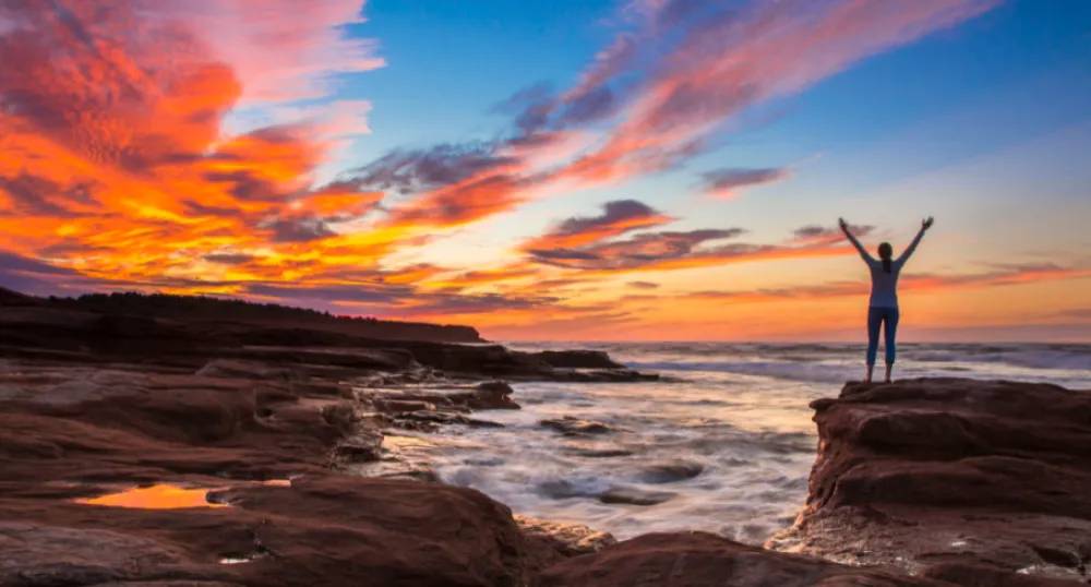 image of a person standing on a rock beach cliff during sunset