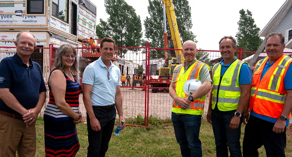 Supporting affordable housing in Alberton image of six people standing in front of a construction area fence with workers in the background