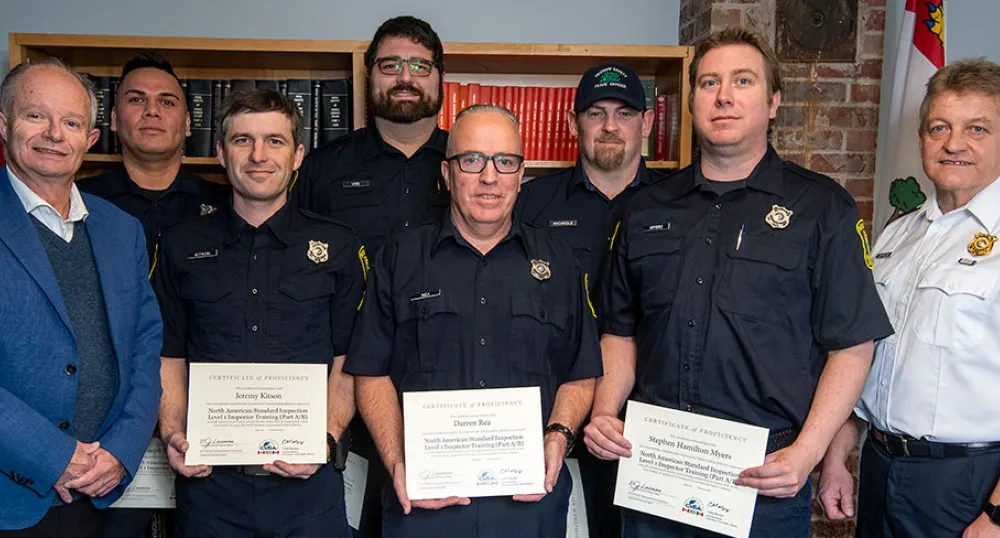 image d&#039;un groupe de personnes dans une pièce, debout côte à côte avec des certificats de détention et des bibliothèques en arrière-plan