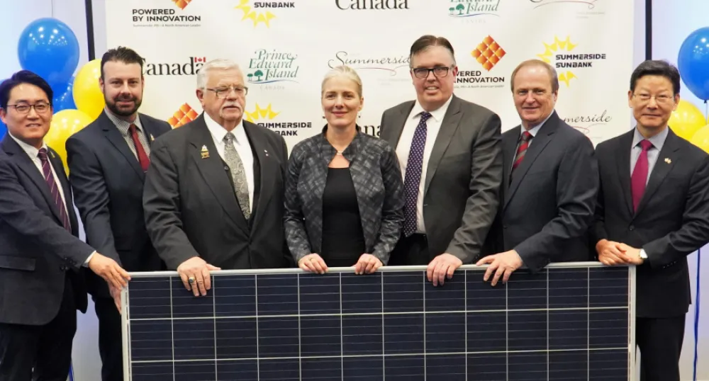 Summerside to benefit from a new solar farm People standing shoulder to shoulder behind a solar panel.