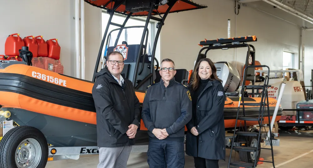 image of three people in front of a small rescue boat inside a garage