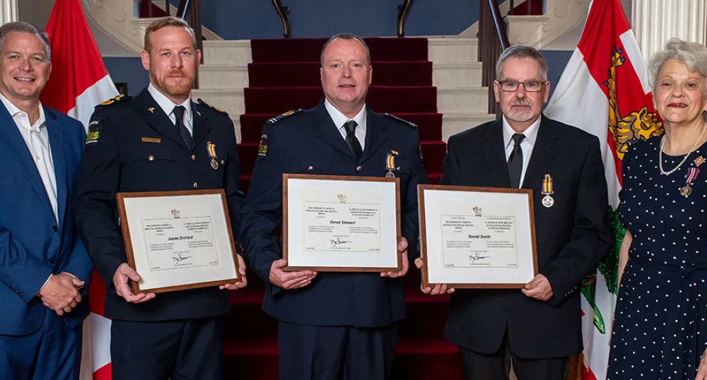 Island paramedics recognized during Paramedic Services Week image of five people standing shoulder to shoulder with the middle three holding framed certificates