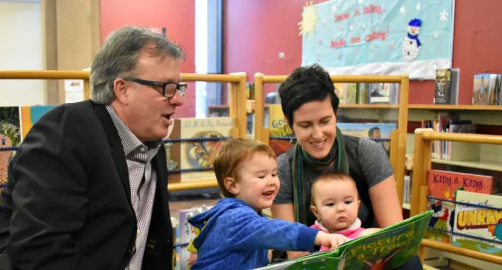 Minister Doug Currie reads a story with Charlie and Rosie and their mother Jinny Greaves.