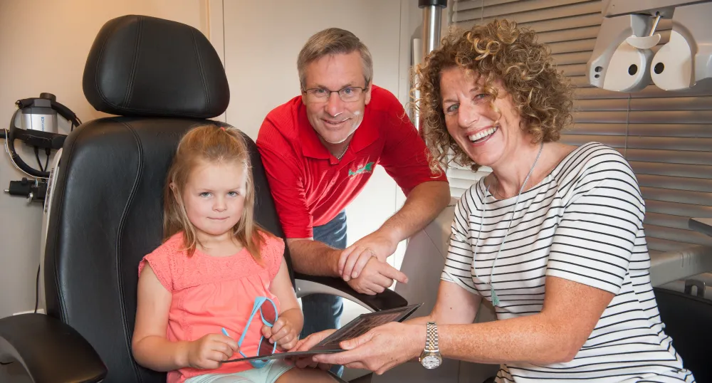 Minister Henderson, and Dr. Toombs are showing a little girl some eye glasses.