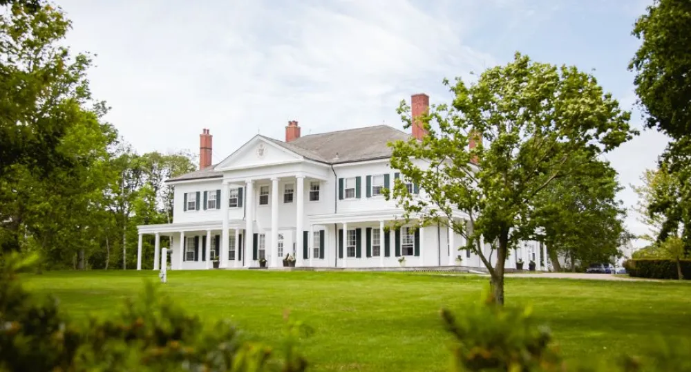 image of a large stately home with a large grass area and various trees surrounding it.