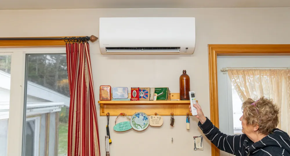 image of a person inside a house using a remote control to use a heat pump