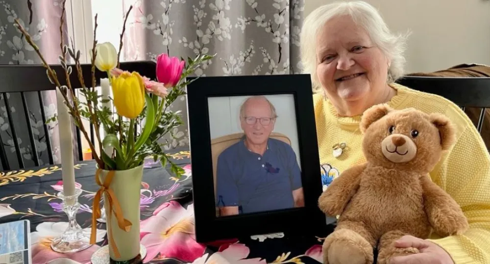 Karen Wood smiles next to a photo of her late husband, Lawrence