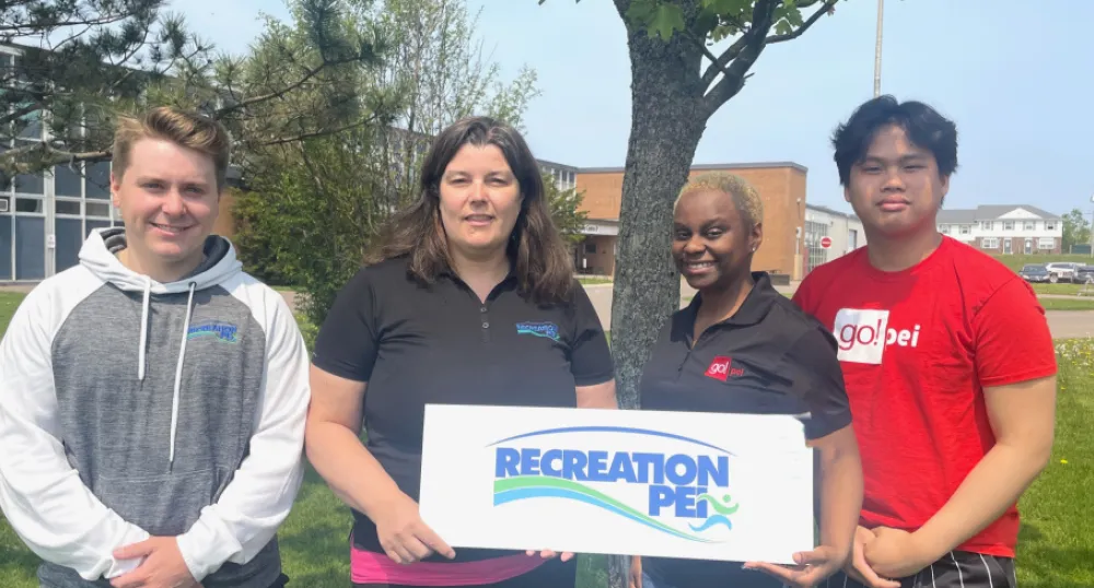Bénéficiaires de microsubventions pour la lutte contre le racisme image de quatre personnes tenant une petite pancarte avec un petit arbre et une école en arrière-plan