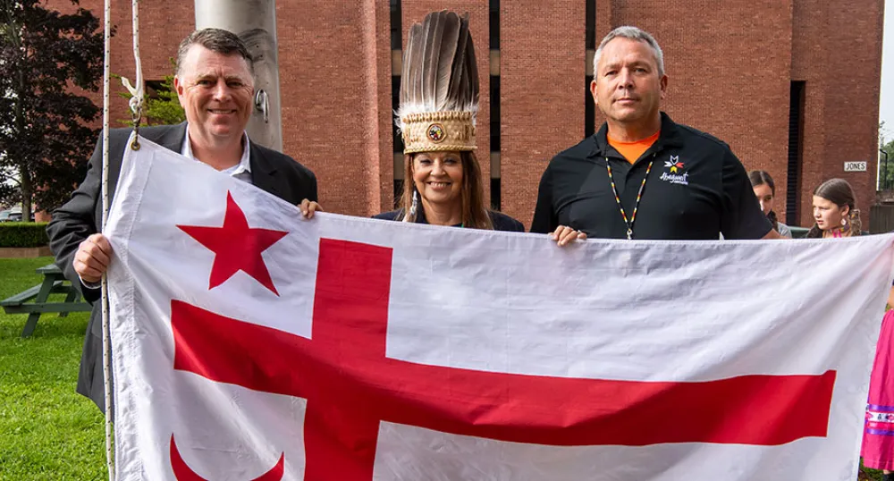 Province celebrates Treaty Day image of three people standing shoulder to shoulder holding a flag in front of them