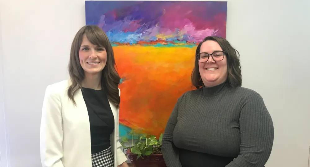 image of two people standing shoulder to shoulder in from of a colourful painting