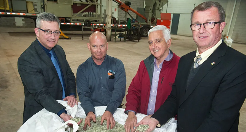 Four people  staqnding behind a large bag of peas.