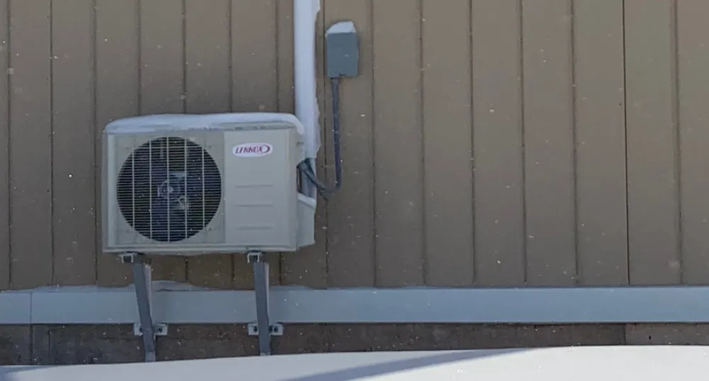 Photo of a PEI house featuring the outdoor unit of a heat pump with snow on the ground
