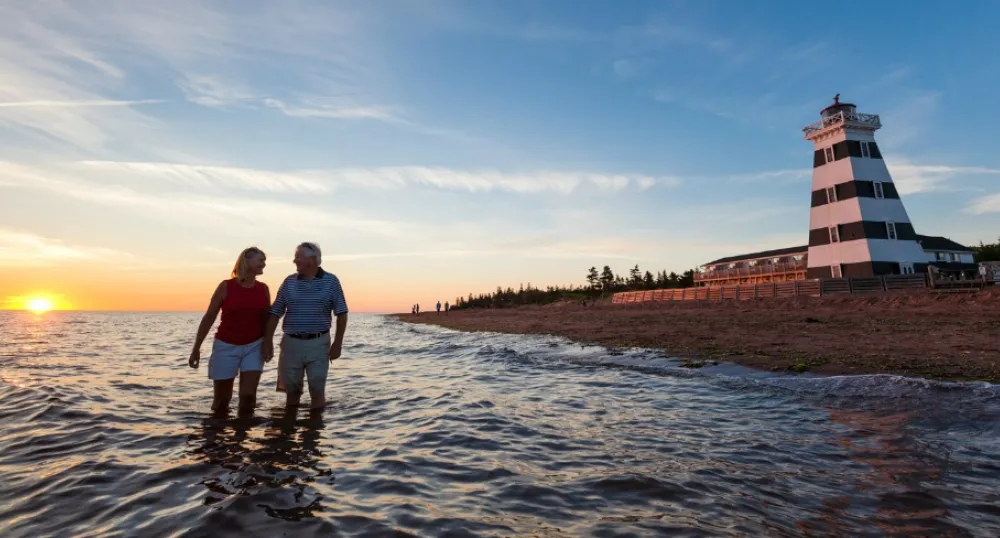 Photo shows a couple strolling on the beach near the West Point Lighthouse.