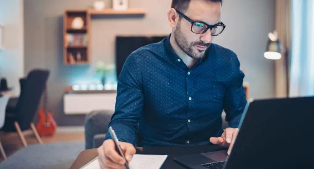 man looking at a computer and writing something down on a notepad