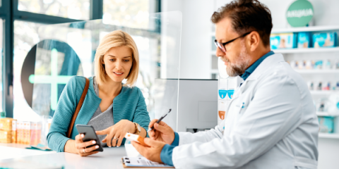 Pharmacist assisting a smiling woman holding her phone at the counter.