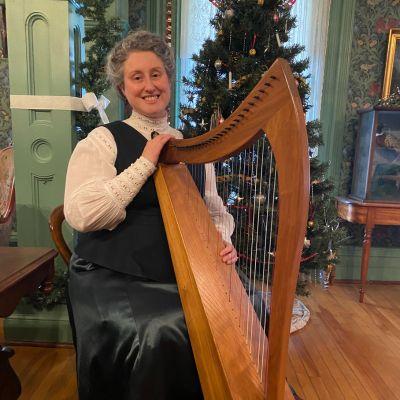 image of a person in 1800s clothing playing a harp in a period room decorated for Christmas