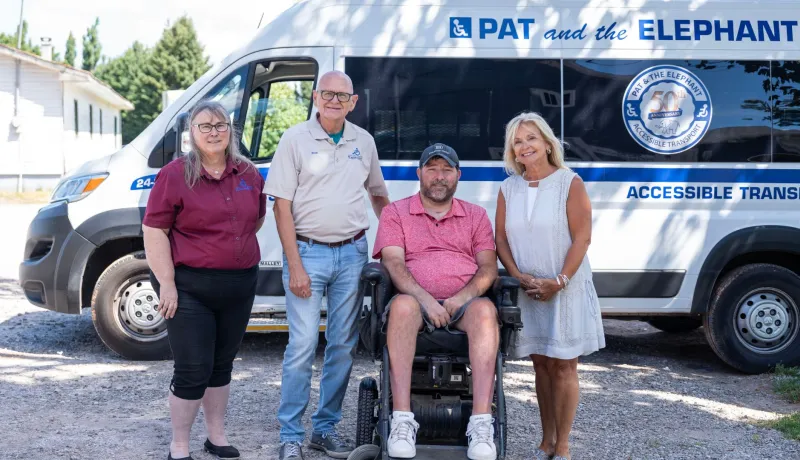 Three people stand around a man in a wheelchair in front of a Pat and the Elephant van.