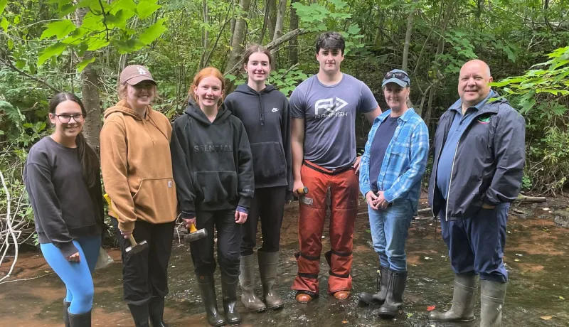 The Minister and watershed staff stand in the river with green foliage behind them.