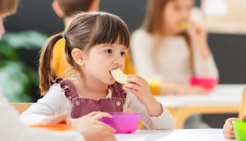 little girl sitting at a table eating a banana