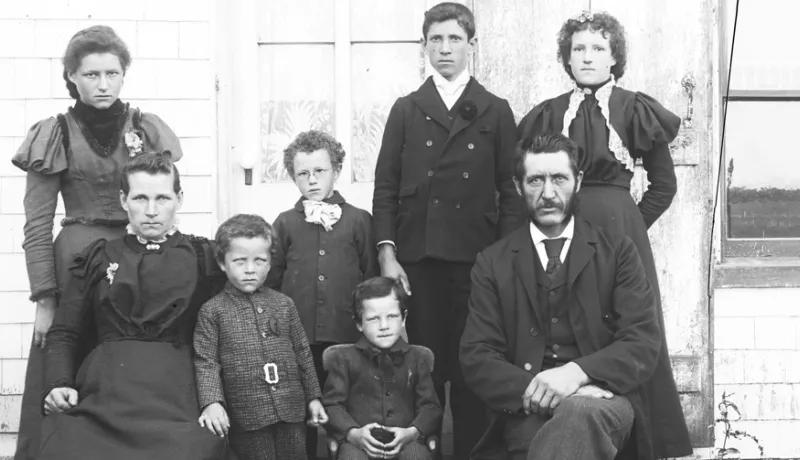Family consisting of a man, woman, and six children posing for photograph in front of a house