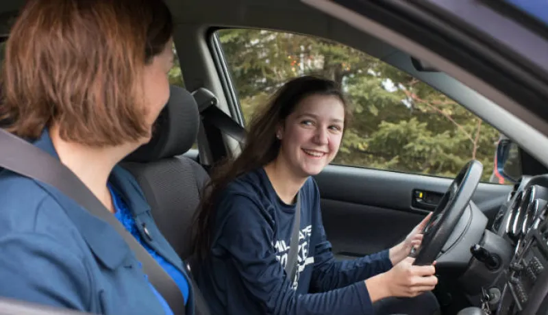 Young driver sits in driver seat with adult on passenger side
