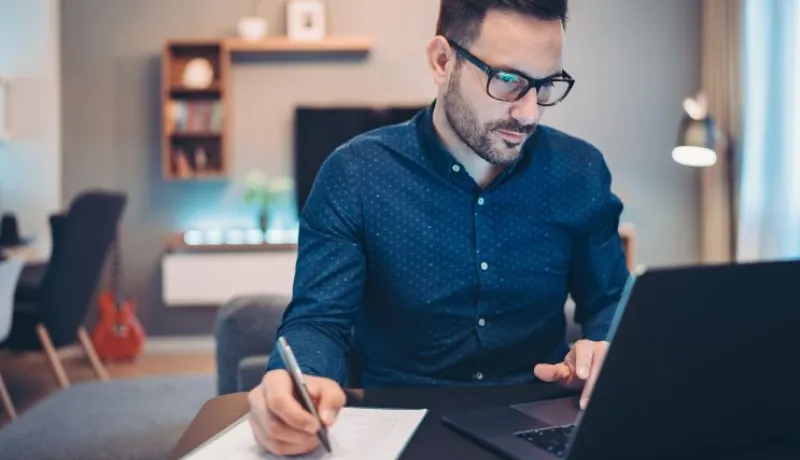 man looking at a computer and writing something down on a notepad