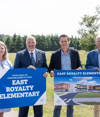 Four people stand in front of the new school site holding signs that depict the future buildings design.