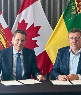 Le premier ministre Lantz et le premier ministre Moe sont assis devant les drapeaux de l'Île-du-Prince-Édouard, de la Saskatchewan et du Canada.